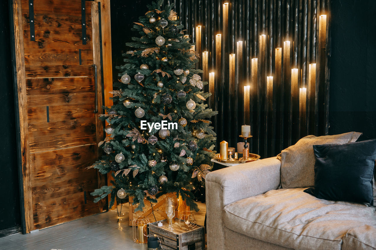 Christmas interior with a beautiful christmas tree, sofa, light bulbs and dark background.