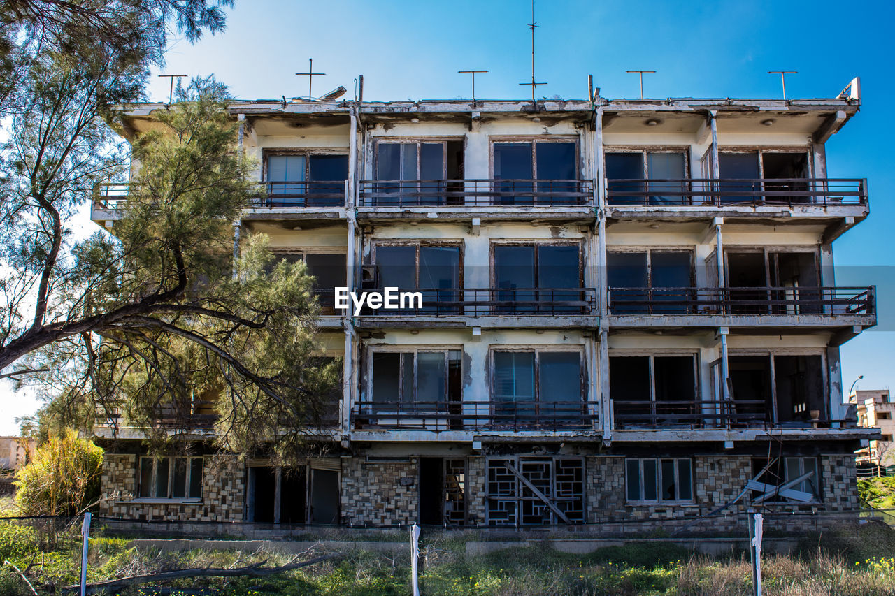 architecture, built structure, building exterior, house, residential area, urban area, building, tree, plant, home, estate, sky, nature, neighbourhood, residential district, no people, facade, city, outdoors, window, abandoned, day, damaged, construction industry, old, rundown, tower block, blue