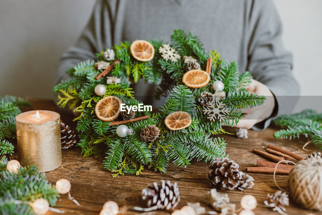 A male florist makes a new year's wreath with fresh fir branches, pine cones and dried fruits. 