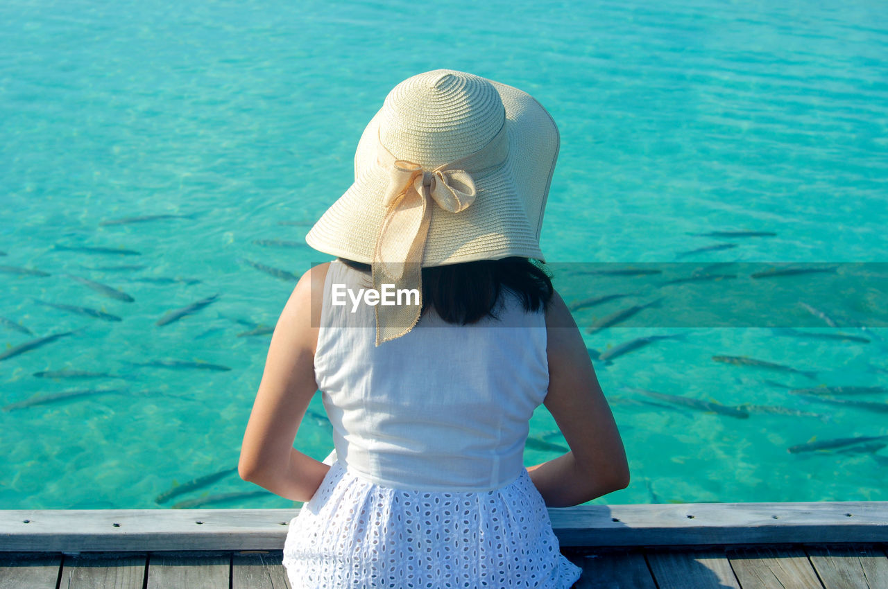 Rear view of woman looking at fish swimming in sea