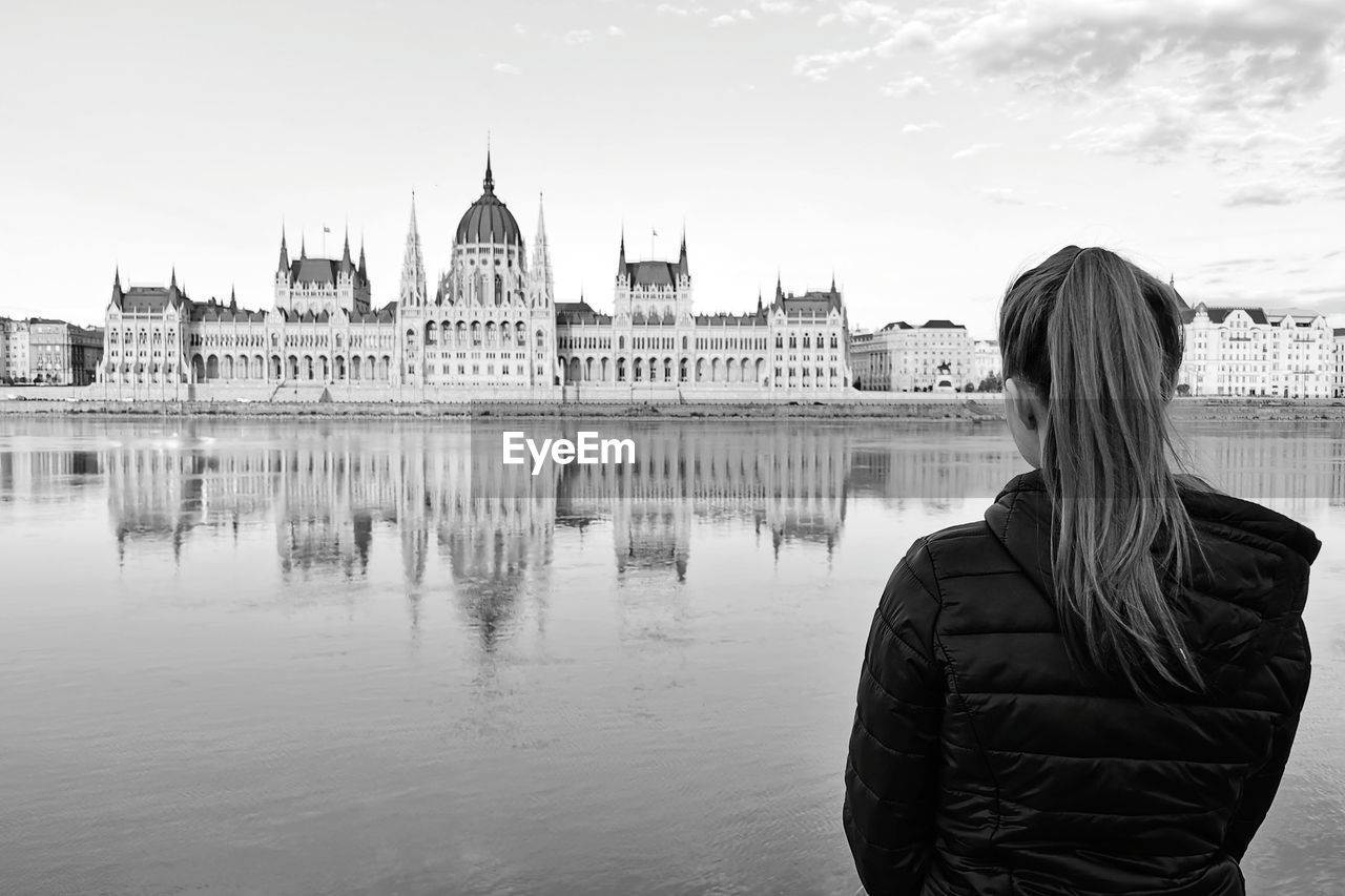 Rear view of woman standing by danube river in front of the parlament