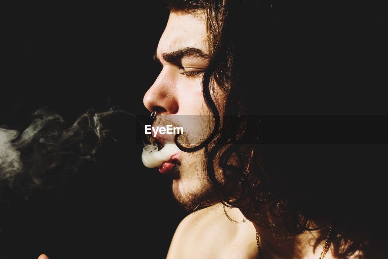 Young man smoking against black background