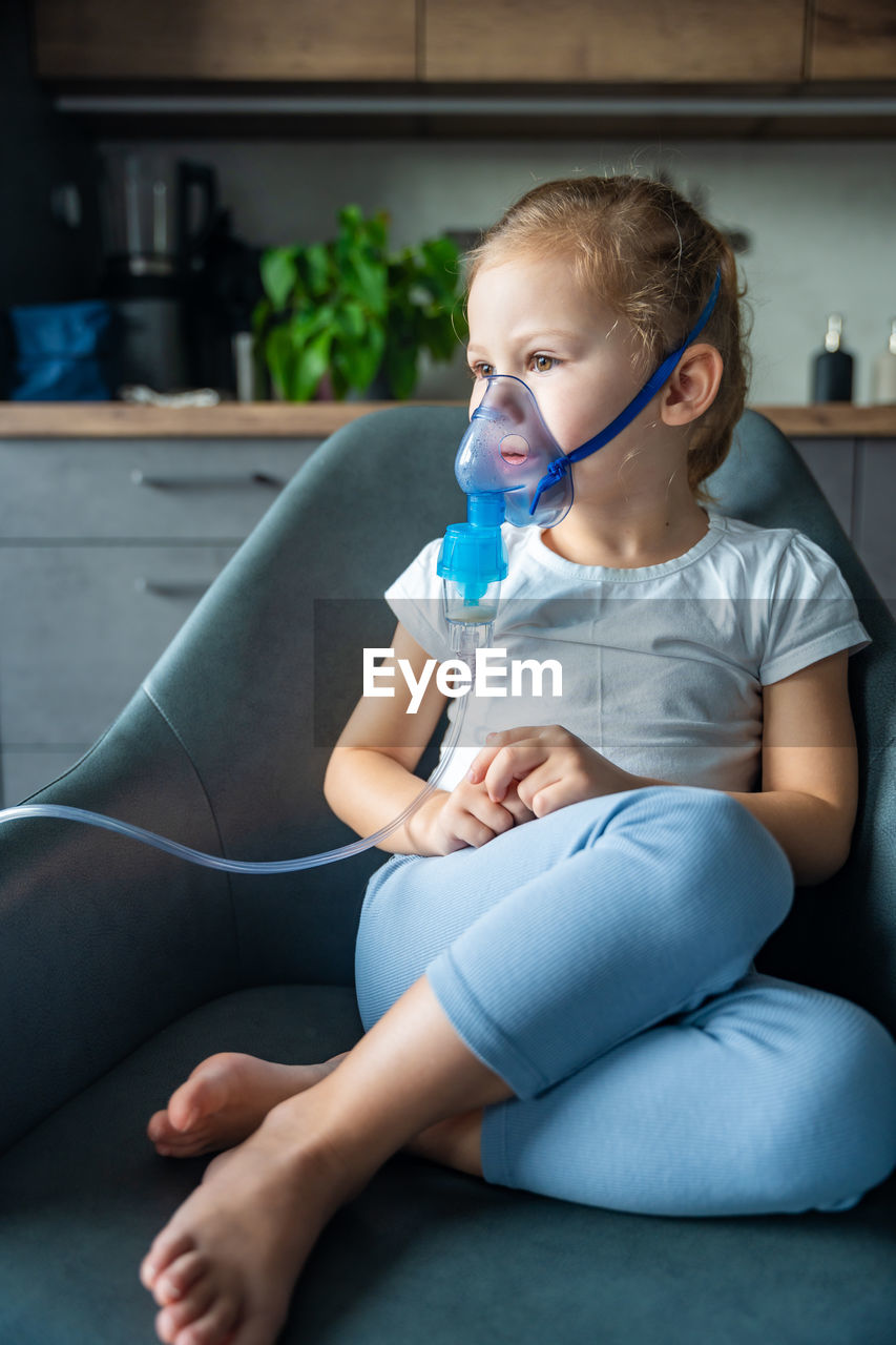 portrait of young woman drinking water while sitting on sofa at home