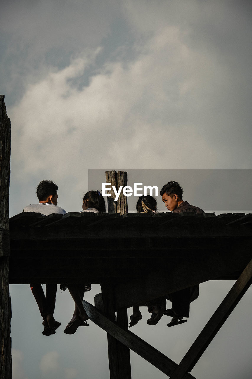 PEOPLE SITTING ON RAILING AGAINST SKY WITH BUILDING