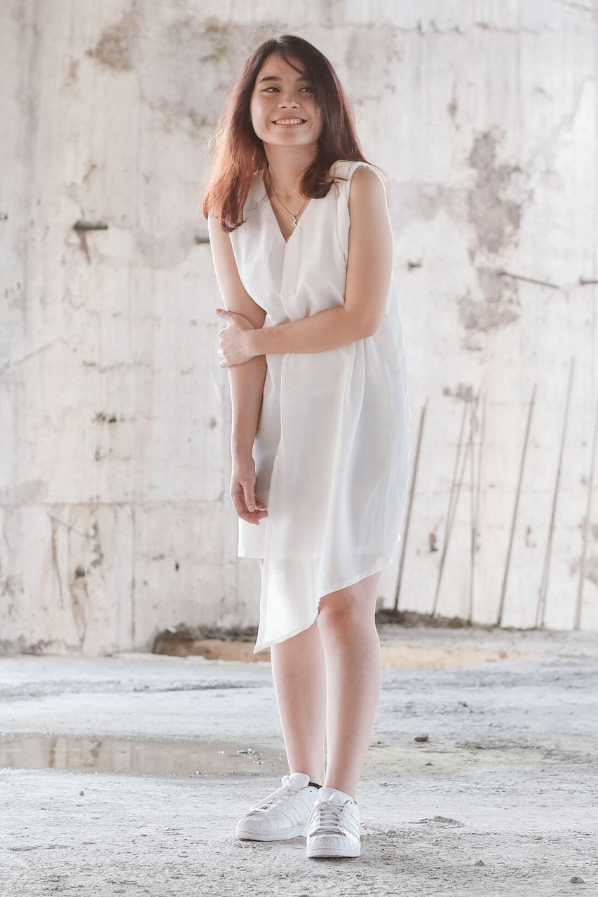 PORTRAIT OF A SMILING YOUNG WOMAN STANDING OUTDOORS