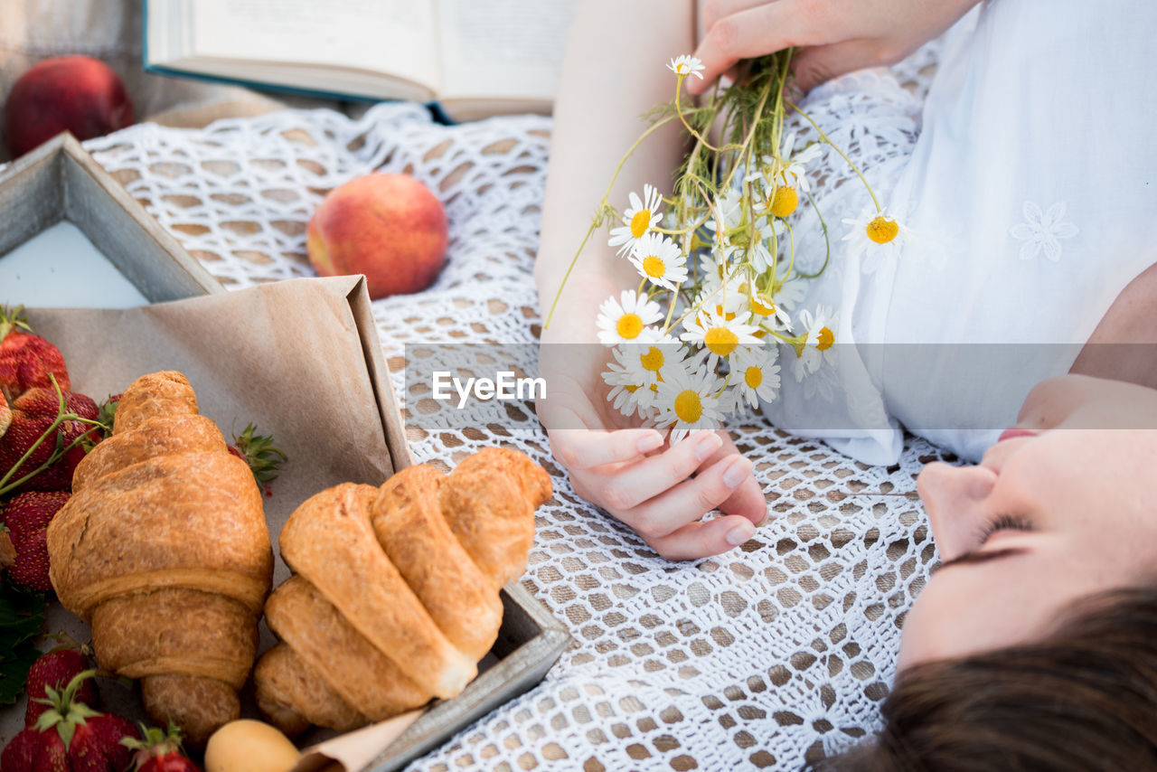 High angle view of woman holing flowers lying on bed with food