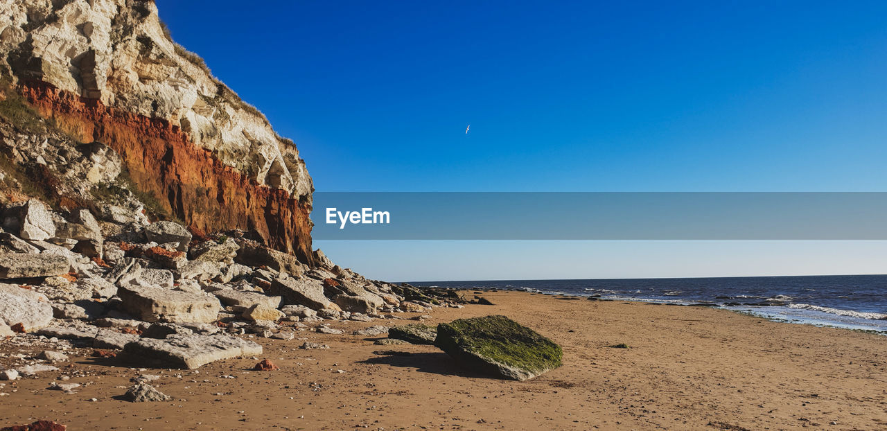 SCENIC VIEW OF ROCKS ON BEACH AGAINST CLEAR BLUE SKY