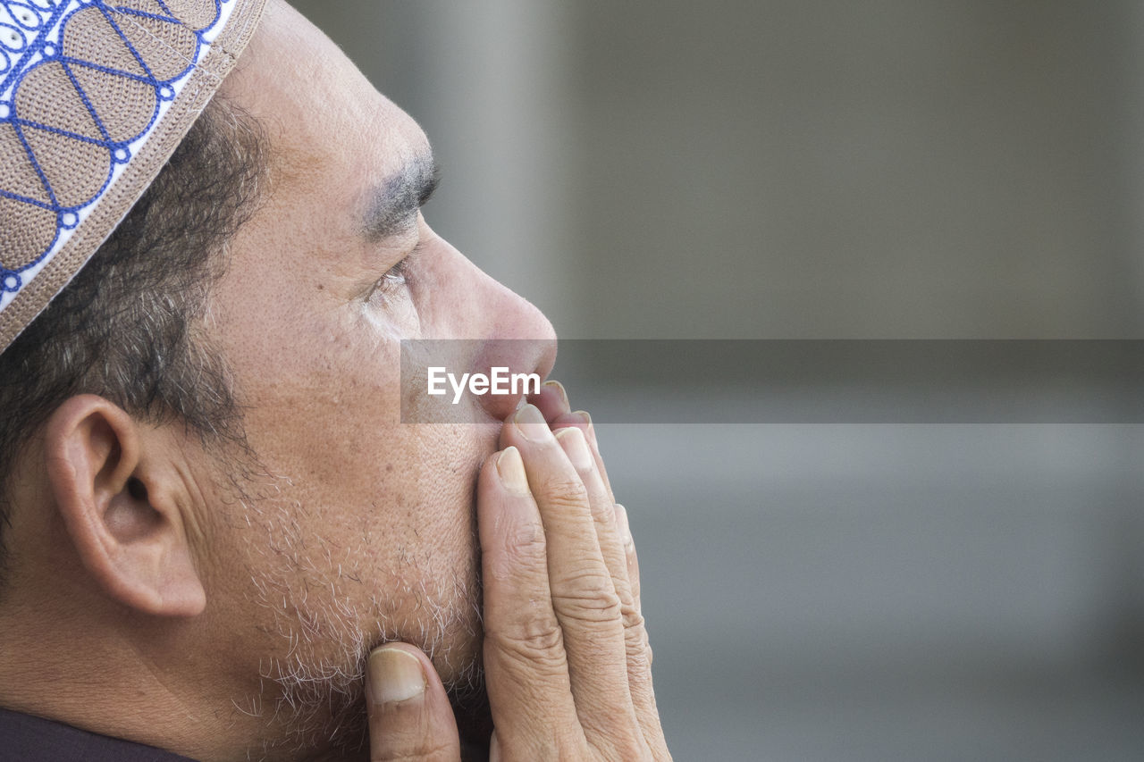 Close-up of mature man praying while sitting at mosque