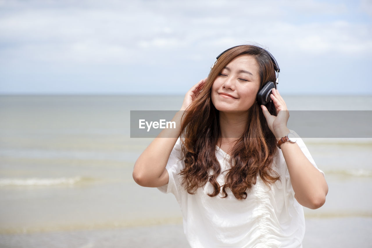 Smiling woman listening to music while standing at beach