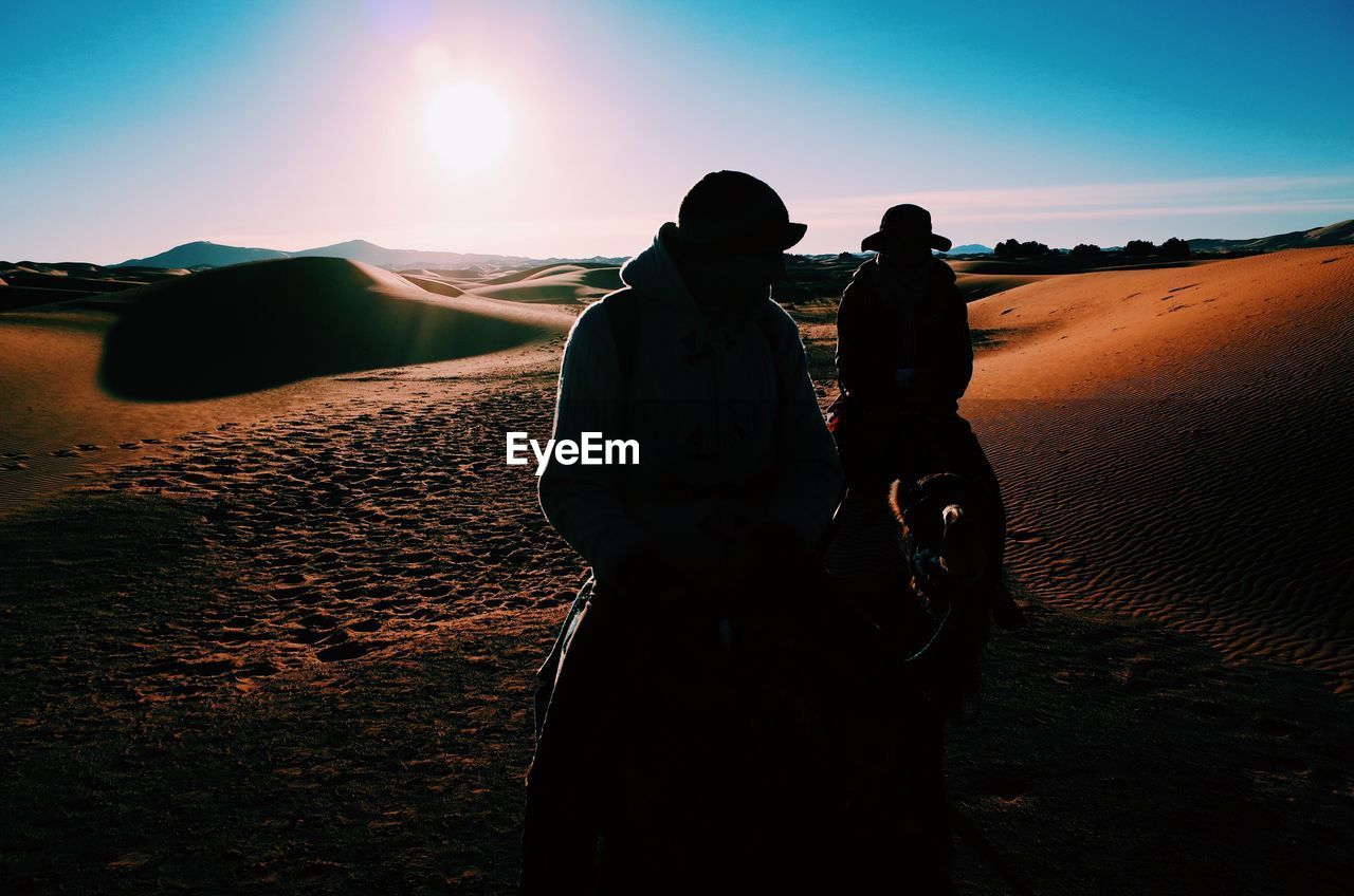 Silhouette men on camels at desert against sky
