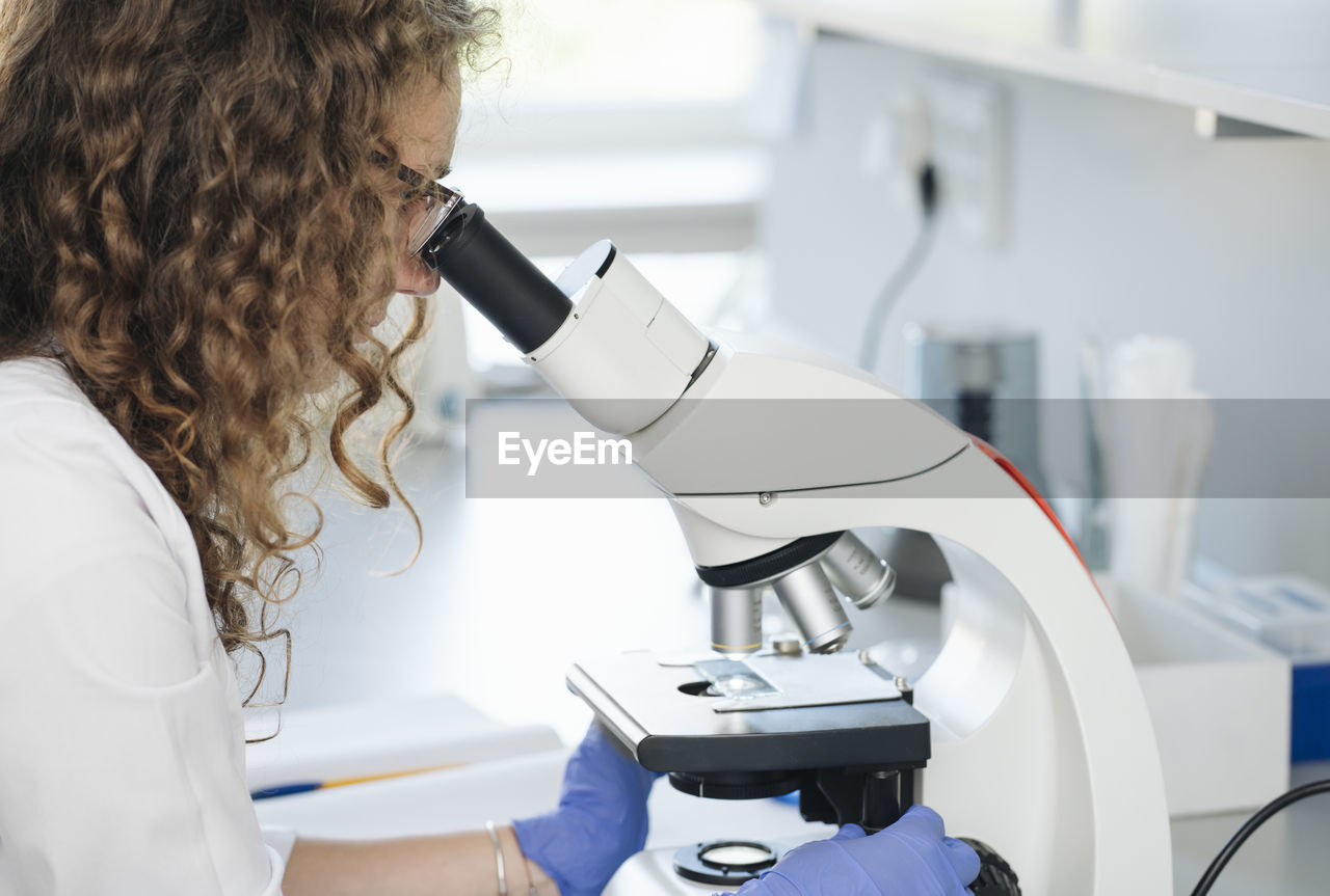 Scientist researching on sample through microscope in laboratory