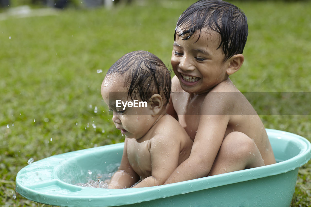 Close-up of siblings playing in bathtub in yard