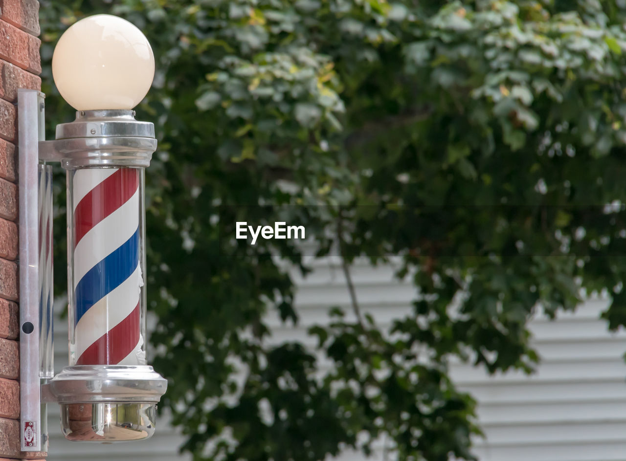 Close-up of barber poll in front of trees.