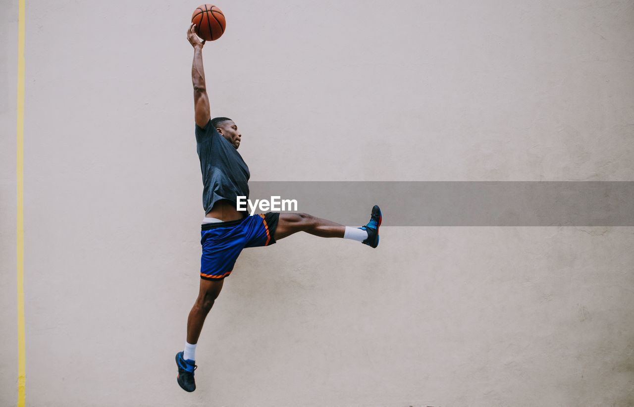 Young man playing basketball against wall