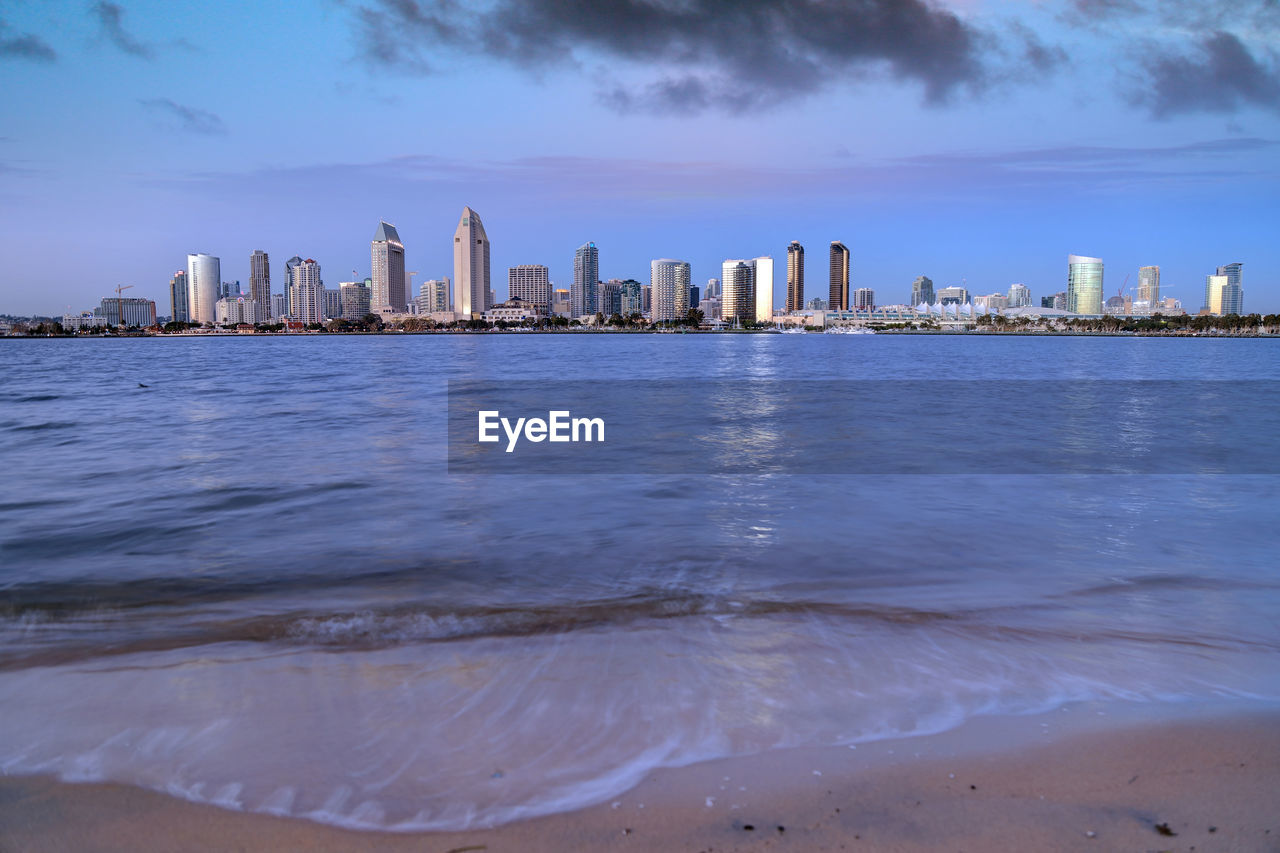 Sea by modern buildings in city against sky