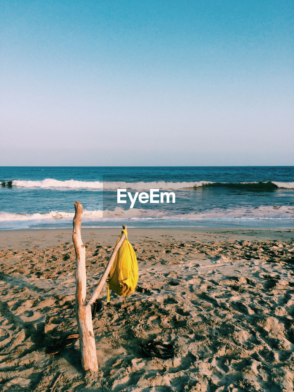 Backpack hanging on driftwood at beach against sky