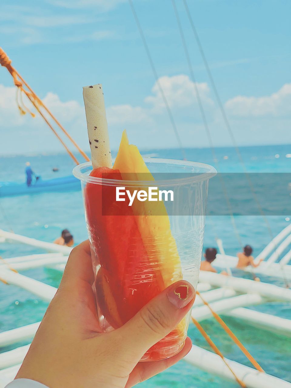 CLOSE-UP OF WOMAN HOLDING ICE CREAM OVER SEA AGAINST SKY