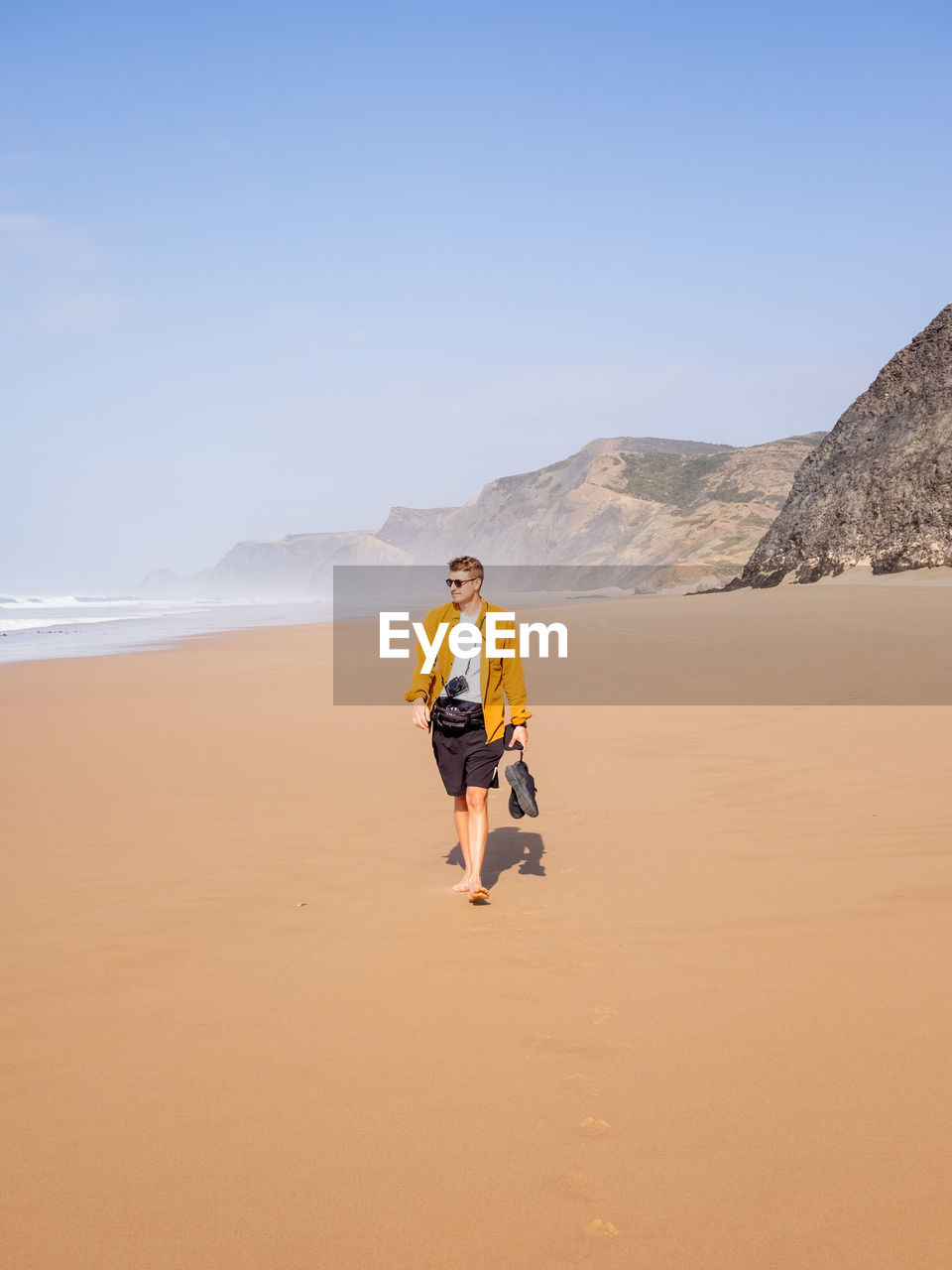 Rear view of man walking on sand at beach against sky