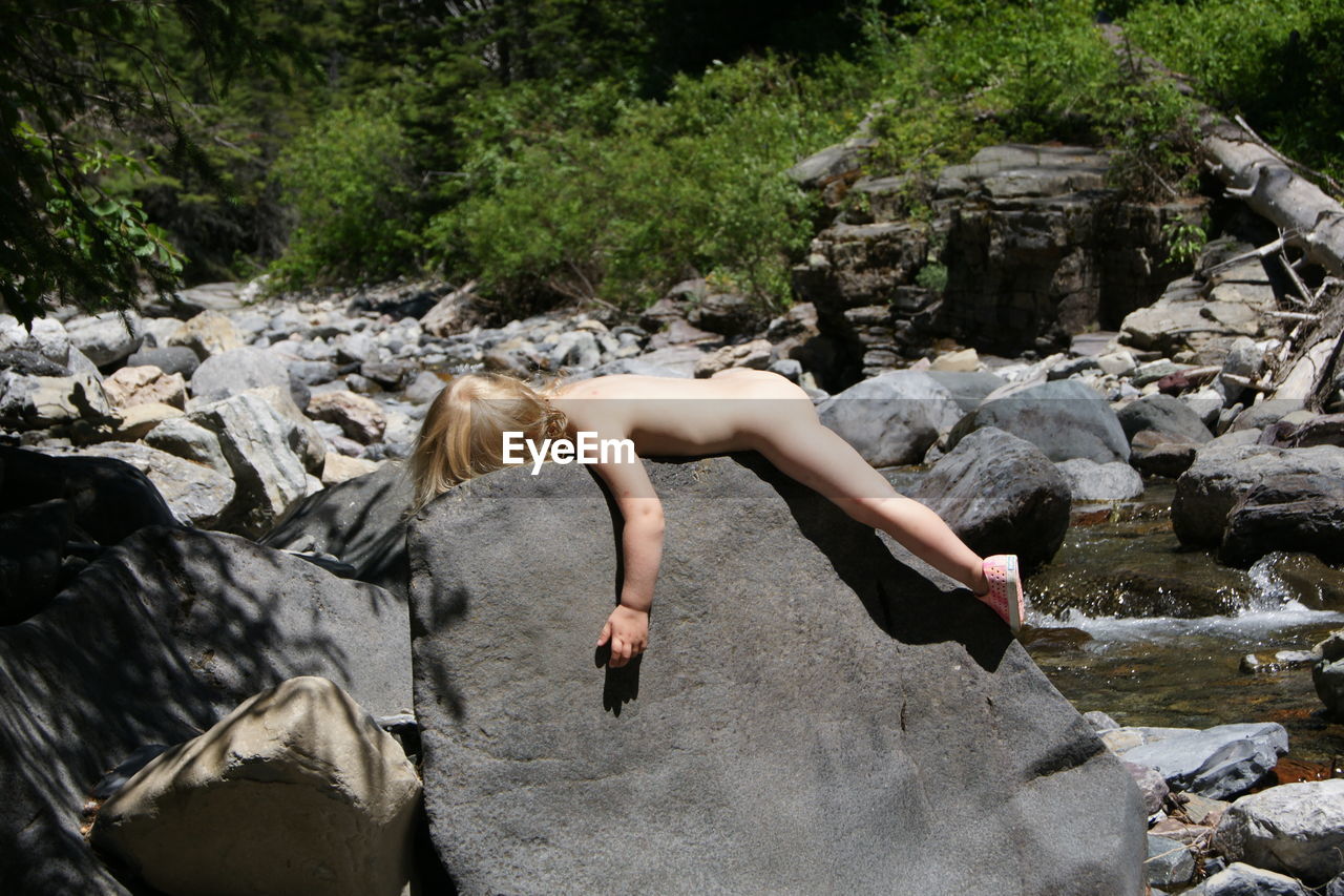 Side view of naked girl lying on rock formation