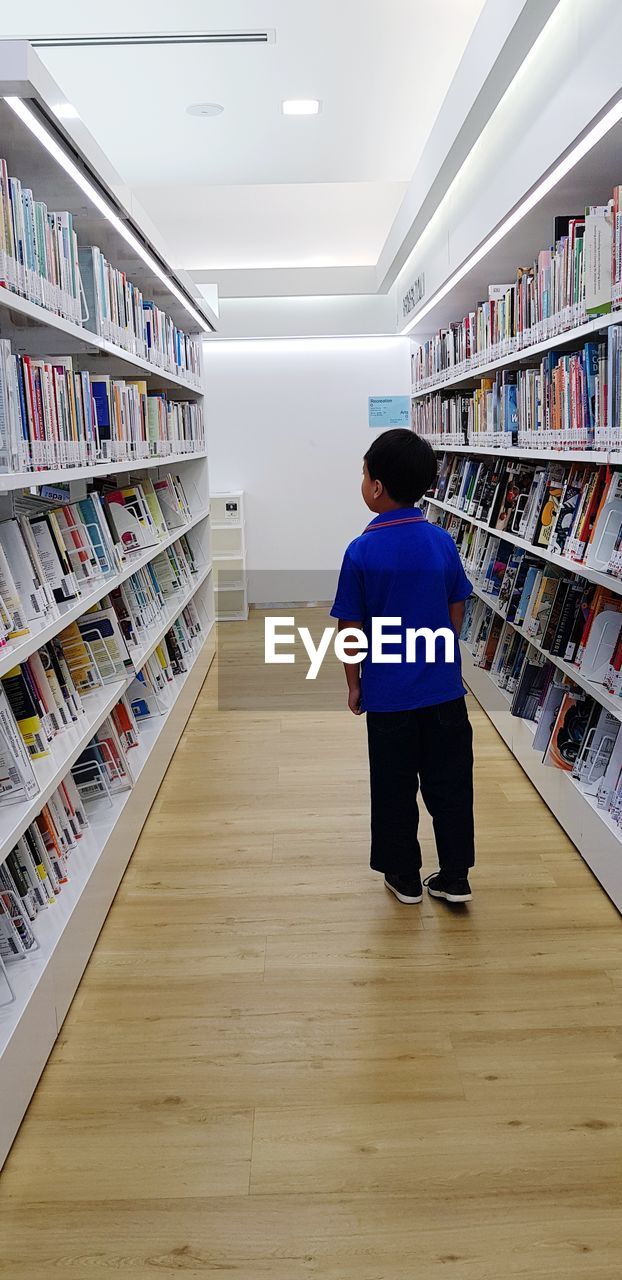 FULL LENGTH REAR VIEW OF MAN STANDING ON BOOKS