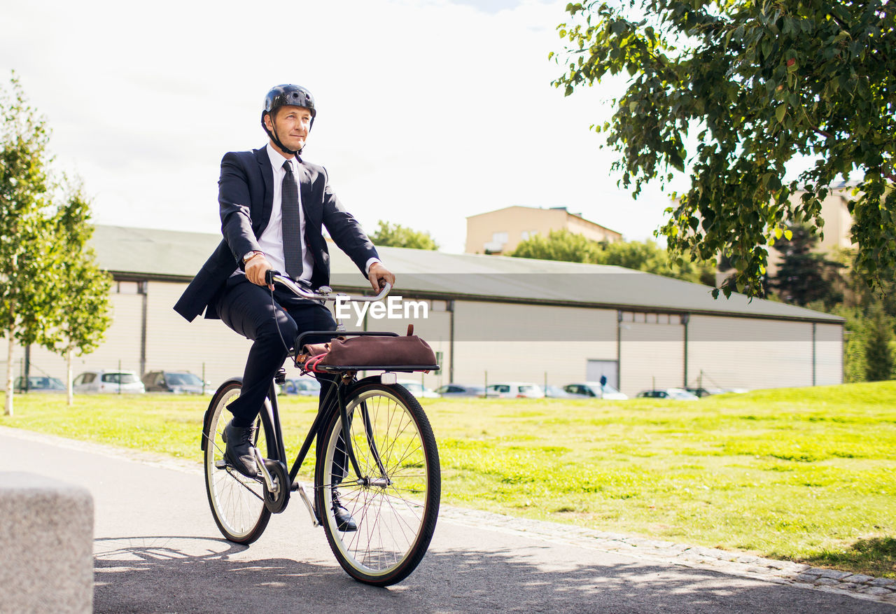 Full length of businessman riding bicycle on street against sky