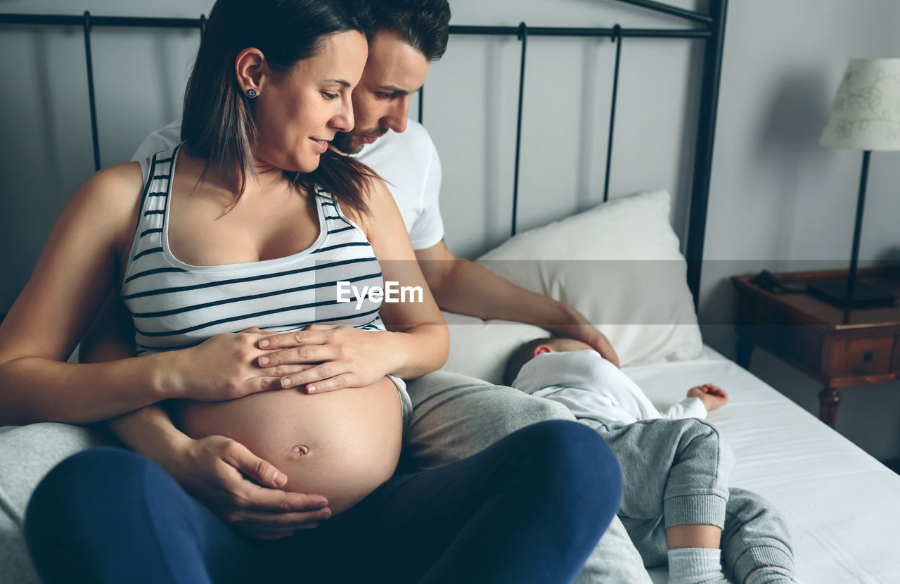 Close-up of man and woman sitting with baby on bed at home