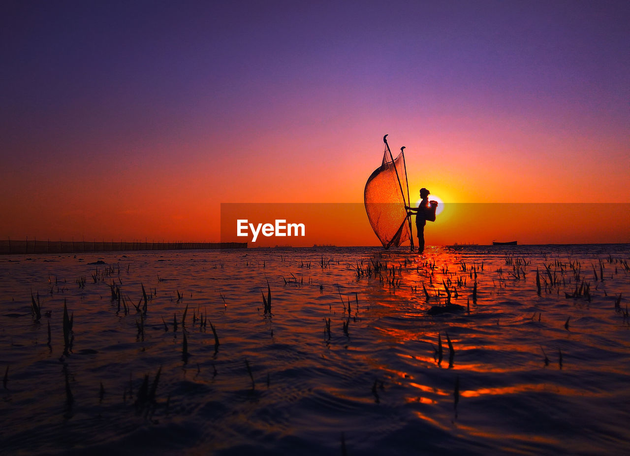 Silhouette man fishing by sea against clear sky during sunset