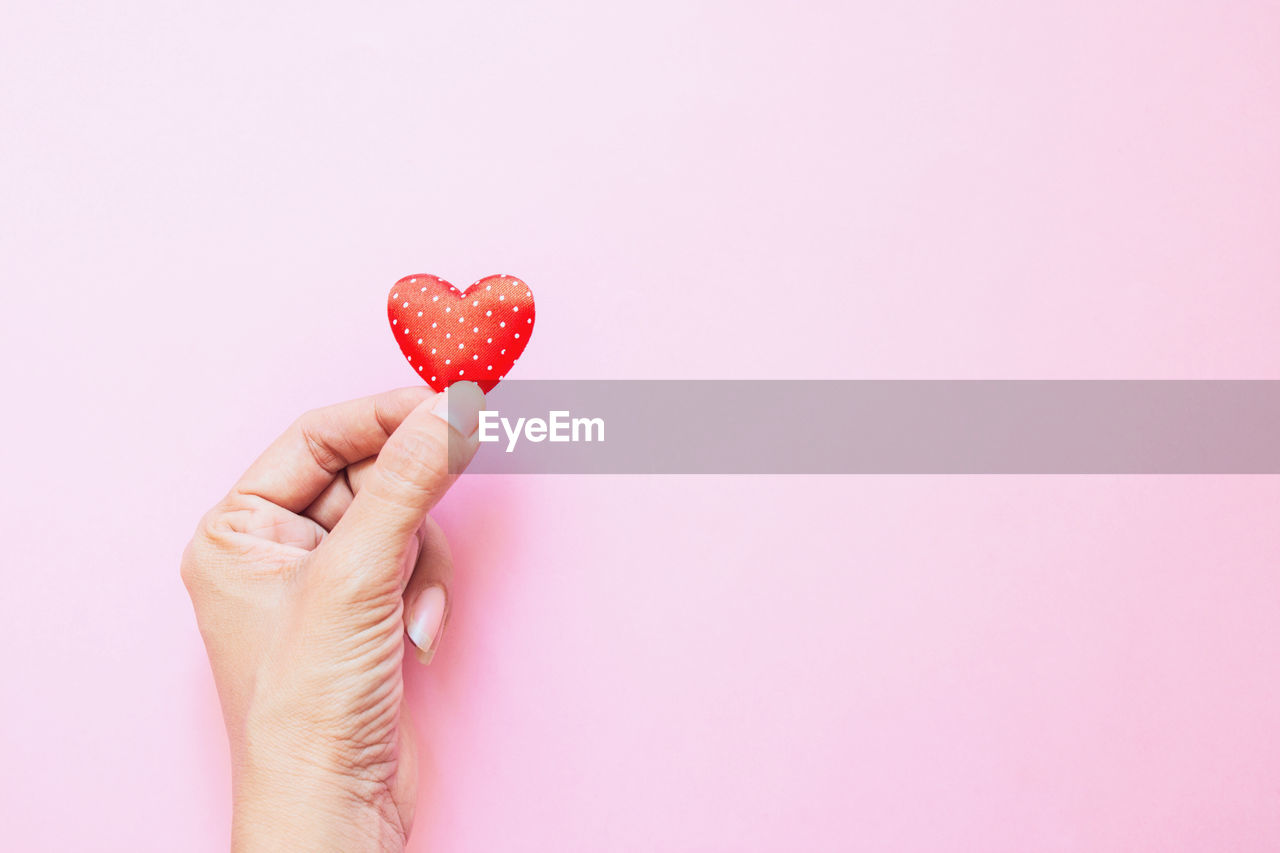 Cropped hand holding heart shape on pink background