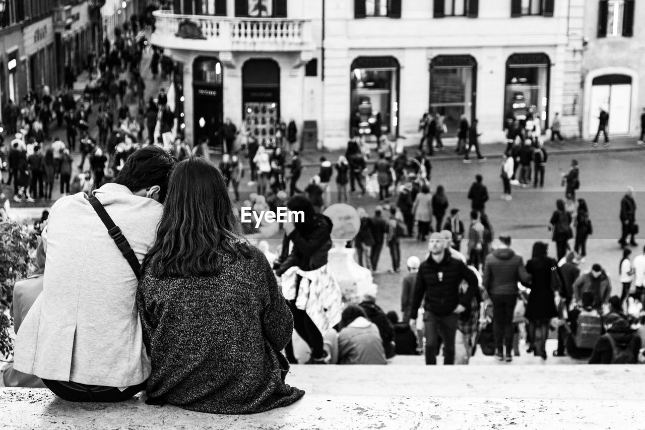 REAR VIEW OF PEOPLE SITTING ON STREET