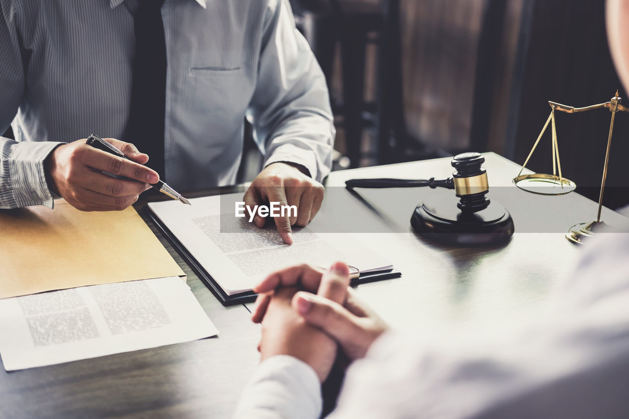 Midsection of lawyer with client on table