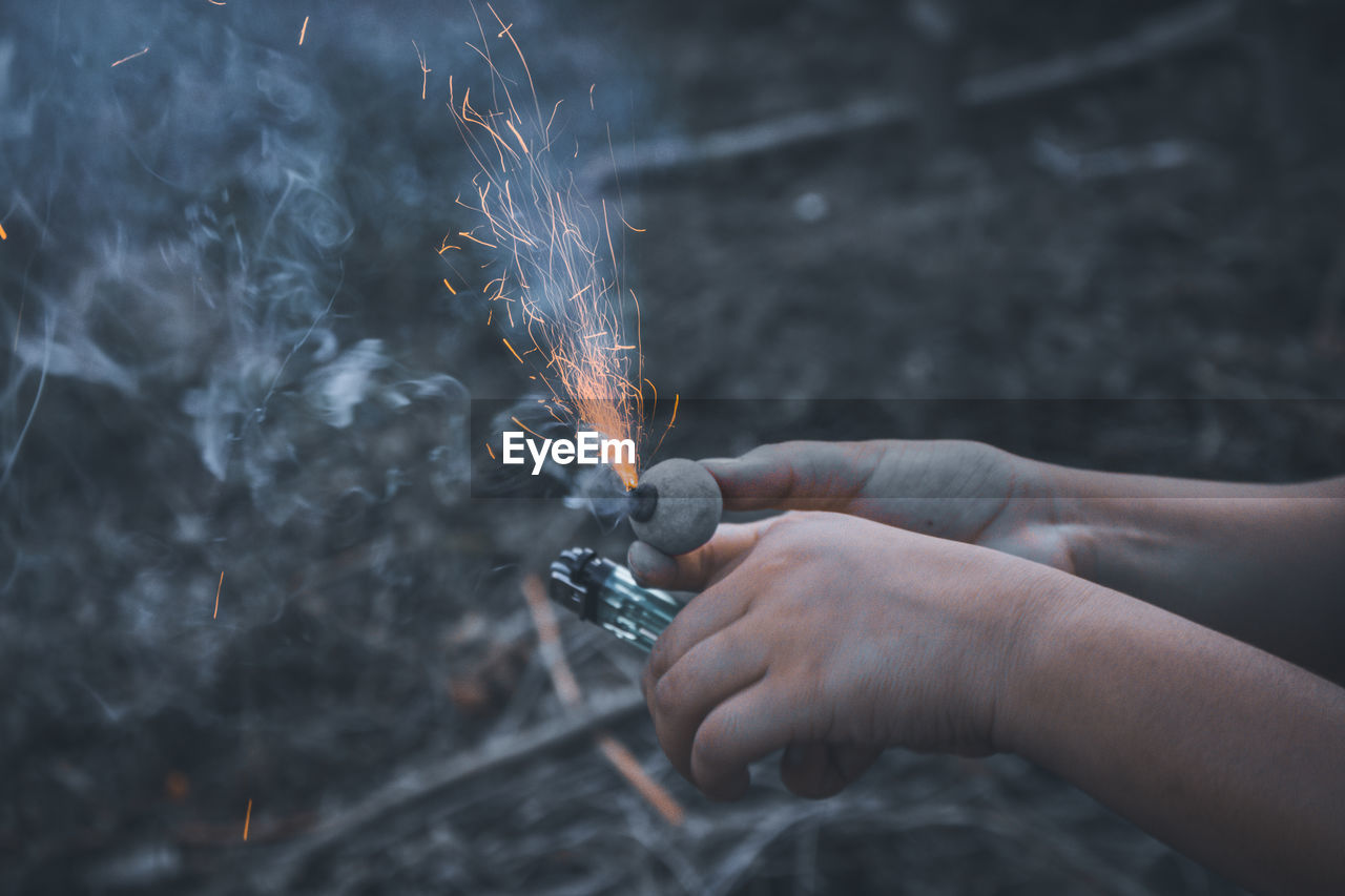 Cropped hands burning firework over field