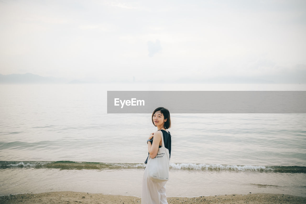 water, one person, sea, sky, adult, beach, nature, land, women, standing, young adult, white, beauty in nature, horizon, tranquility, bride, portrait, dress, scenics - nature, lifestyles, smiling, horizon over water, leisure activity, tranquil scene, emotion, ocean, day, morning, person, happiness, relaxation, copy space, clothing, outdoors, female, casual clothing, sunlight, holiday, contemplation, cloud, vacation, looking at camera, full length, front view, environment, looking, hairstyle, idyllic, wedding dress, trip, long hair, shore, body of water, solitude, three quarter length