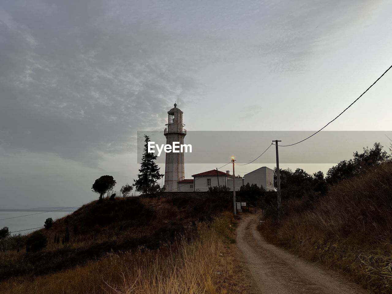 lighthouse, tower, sky, architecture, built structure, building exterior, guidance, building, nature, coast, cloud, plant, sea, morning, hill, travel destinations, horizon, land, no people, water, transportation, tree, road, travel, landscape, environment, security, outdoors, rural area, protection, the way forward, history, grass, tourism, the past, scenics - nature, footpath, dusk, beach, beauty in nature