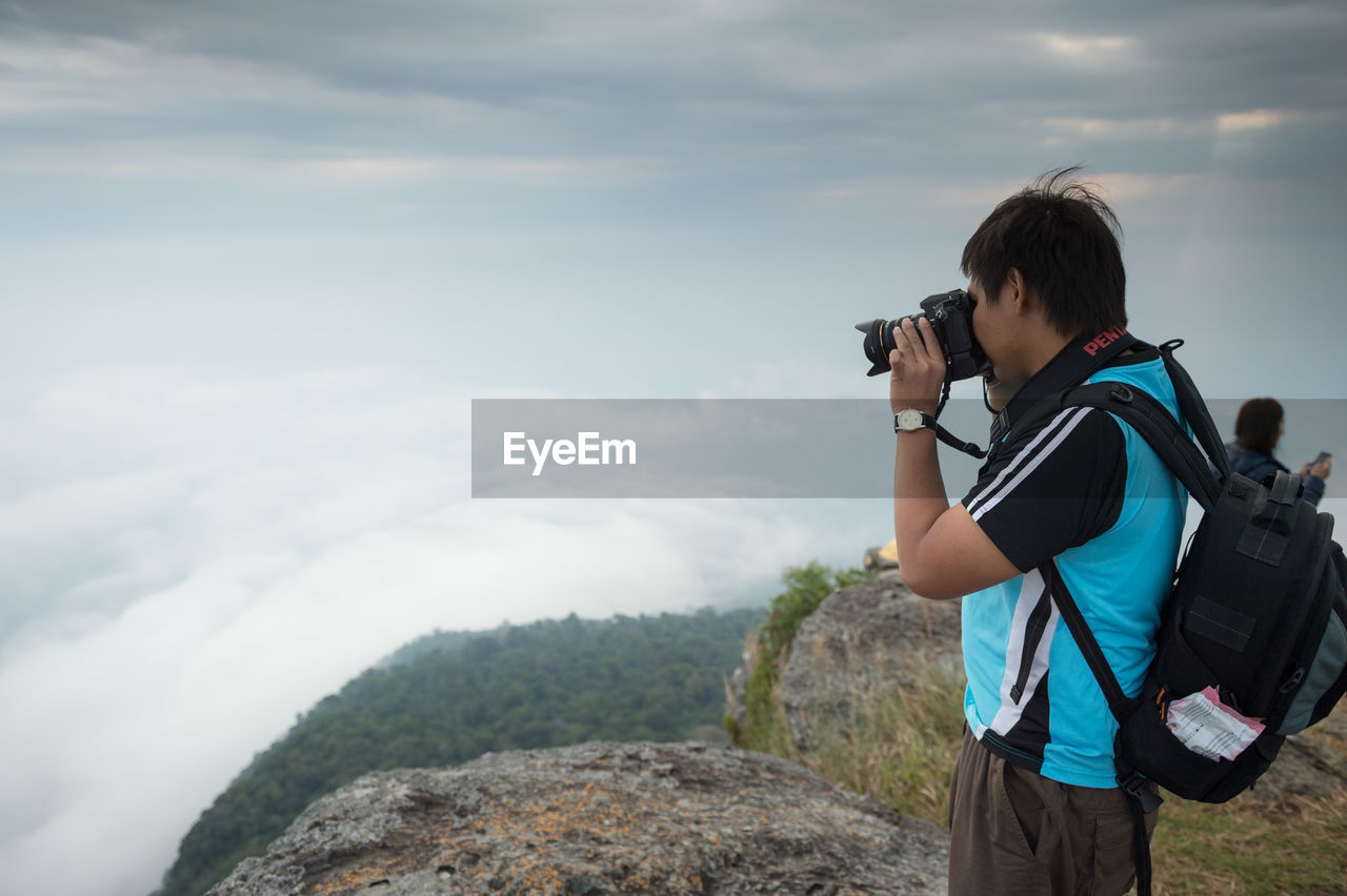 REAR VIEW OF WOMAN PHOTOGRAPHING AGAINST SKY