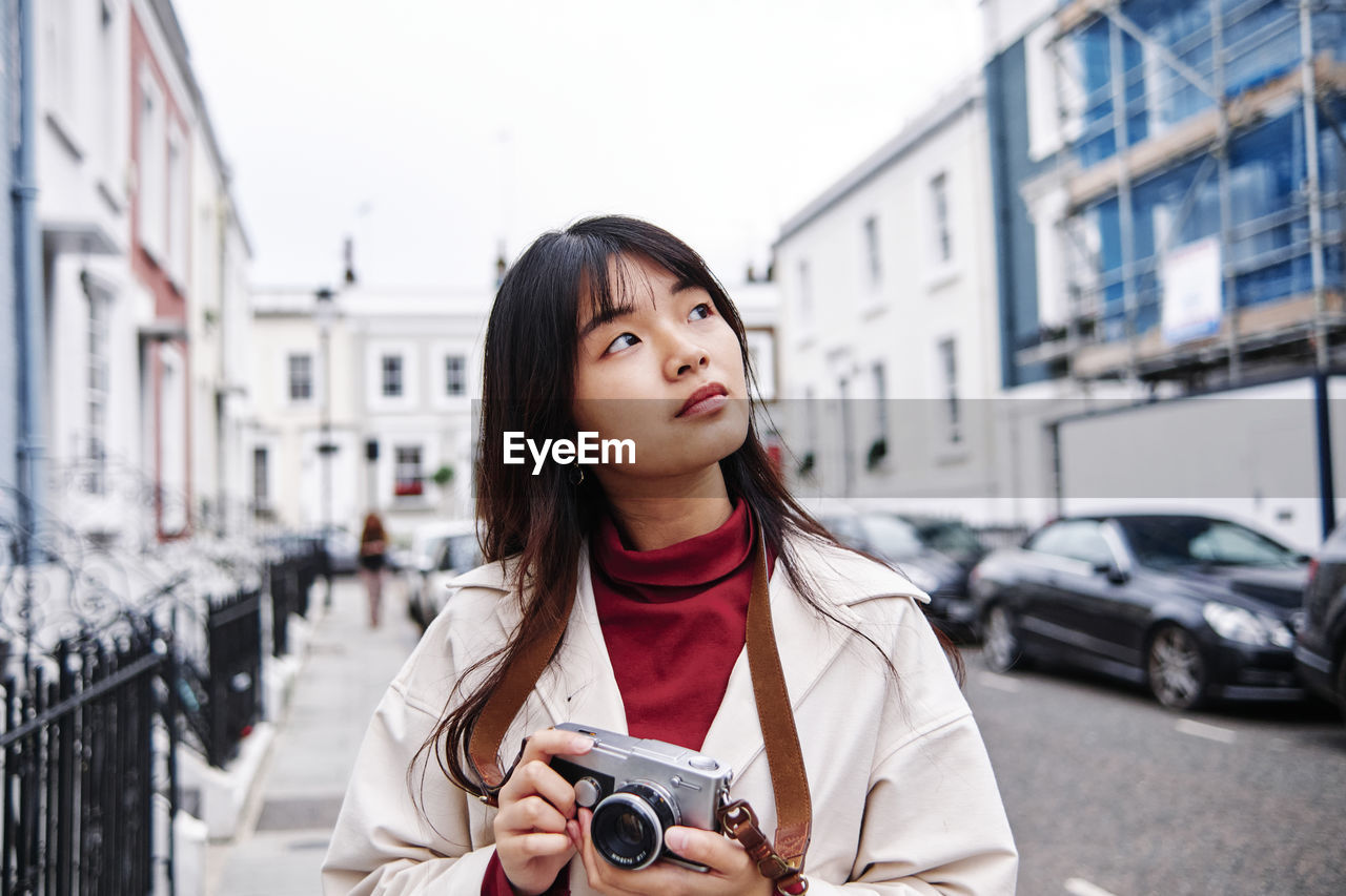 Thoughtful woman holding camera in city