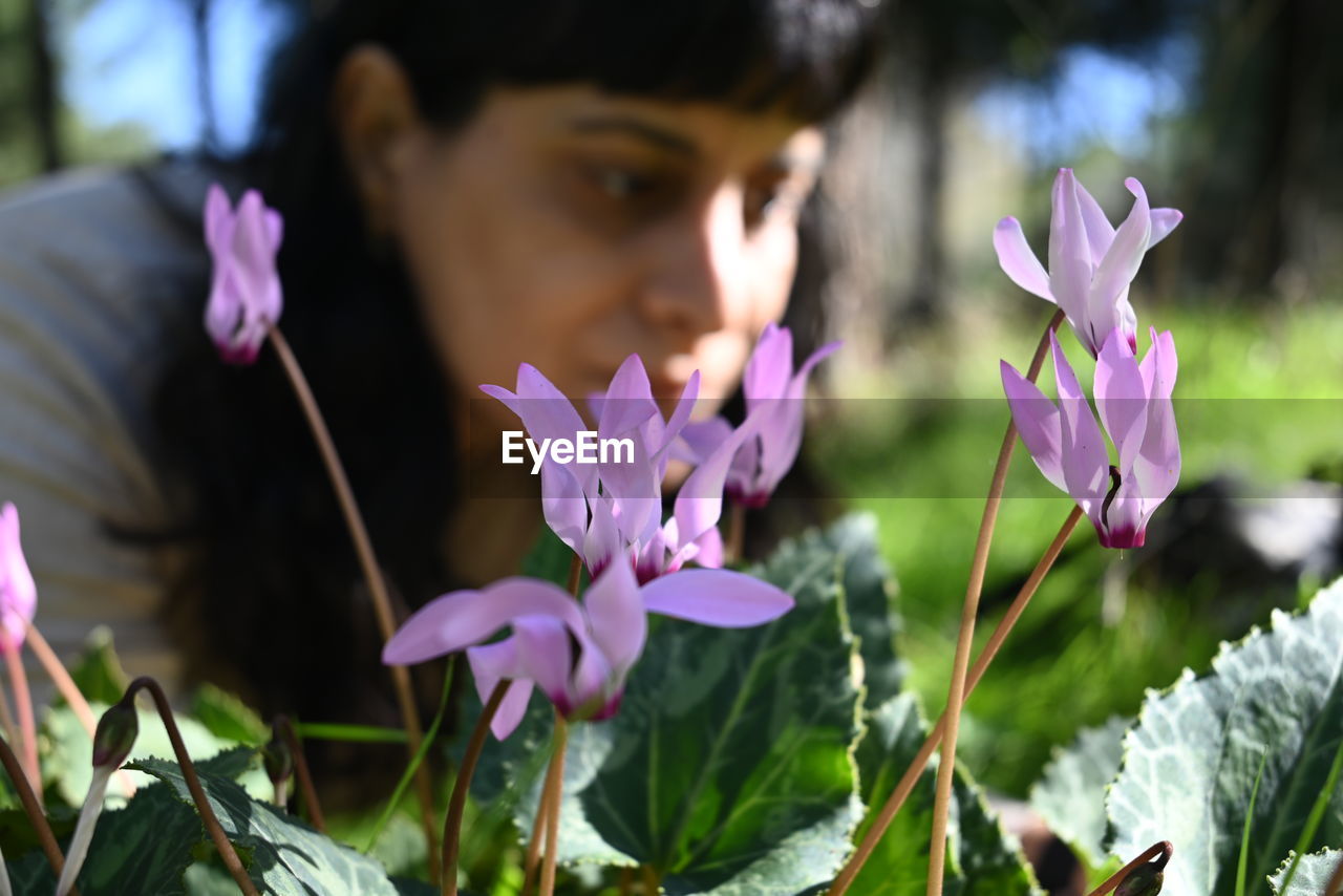 plant, flower, flowering plant, nature, one person, beauty in nature, freshness, purple, human eye, growth, portrait, close-up, fragility, pink, women, headshot, outdoors, day, adult, focus on foreground, young adult, petal, lifestyles, leaf, child, blossom, plant part, selective focus, sunlight, looking, flower head, springtime, inflorescence, female, spring