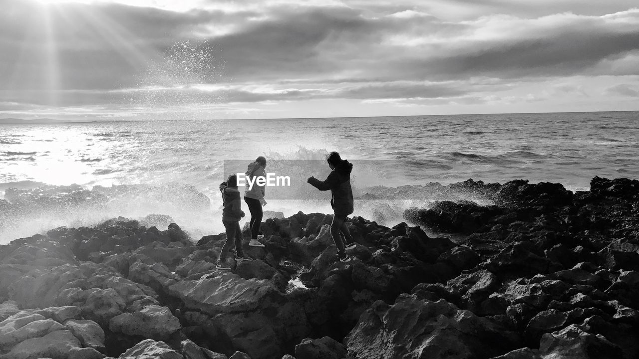 People on rocky shore against cloudy sky