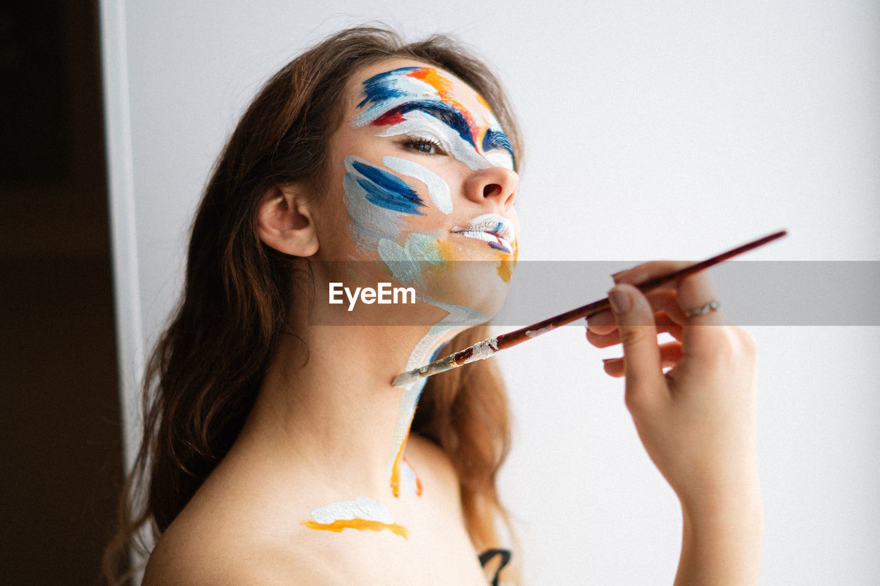 Close-up of woman painting face against wall