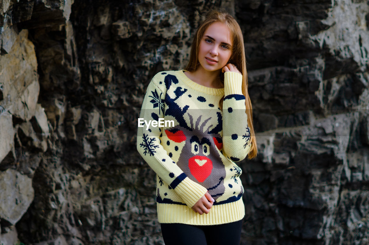 Portrait of young woman standing against rock