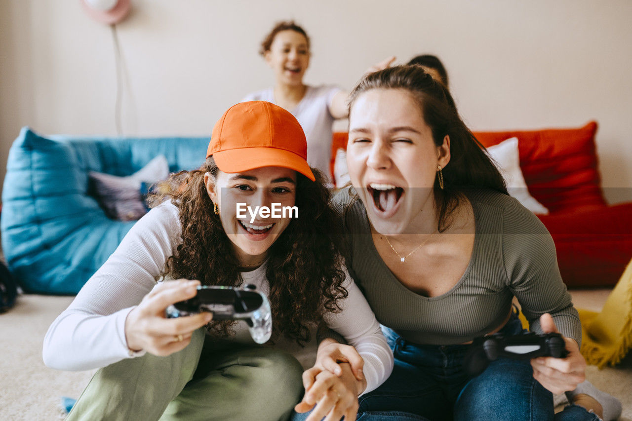 Playful young female friends playing video game at home