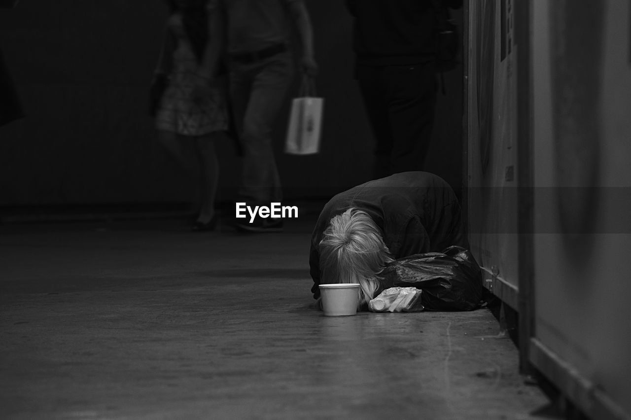 Beggar leaning on floor while people walking in background