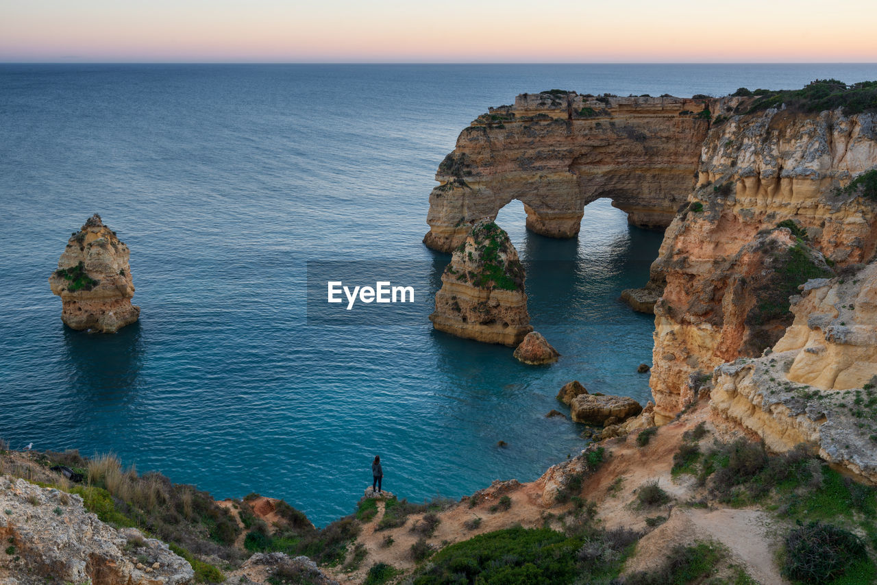 Woman in natural arch cliffs of praia da marinha beach at sunset in lagoa portugal