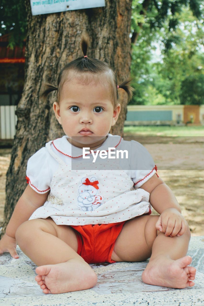 Portrait of baby girl sitting against tree at park