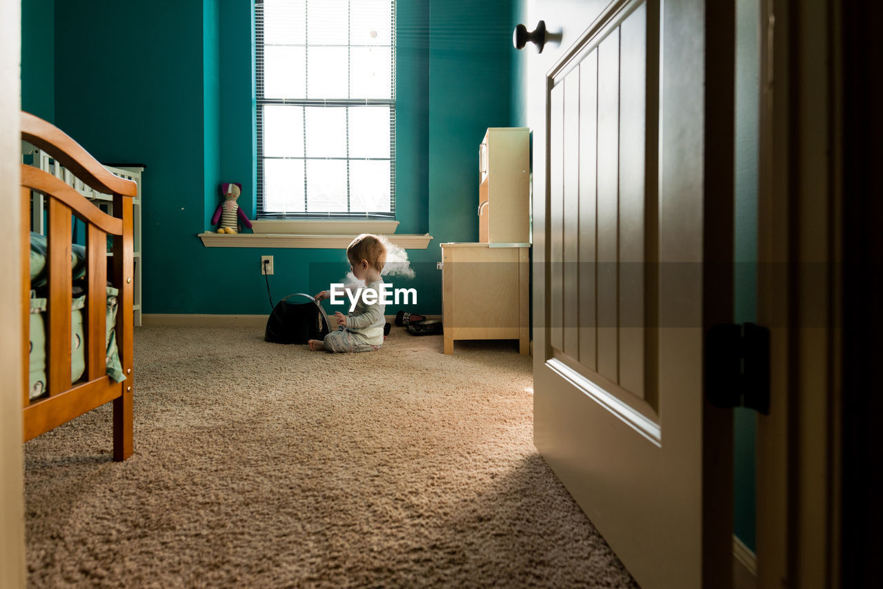 Boy playing with steam machine while sitting on rug at home seen through doorway