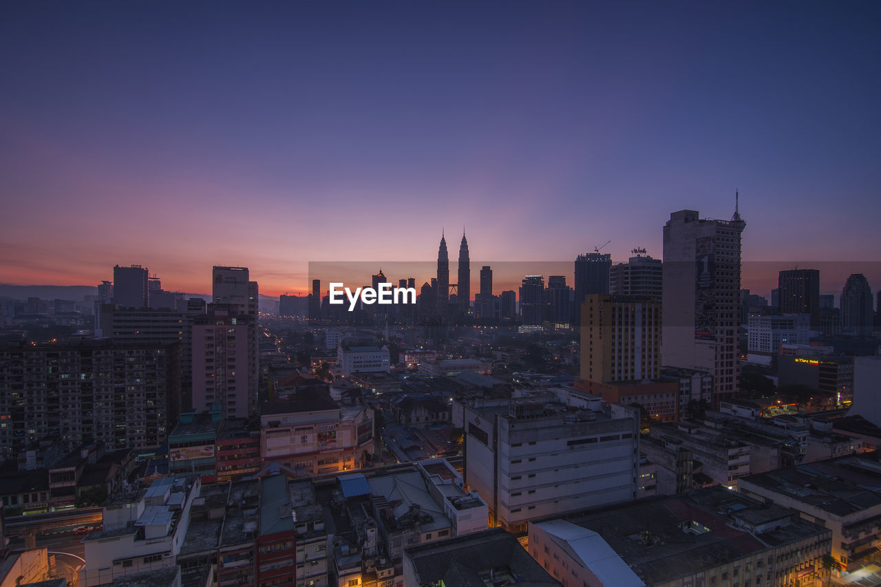 Distant view of petronas towers against sky during sunrise in city