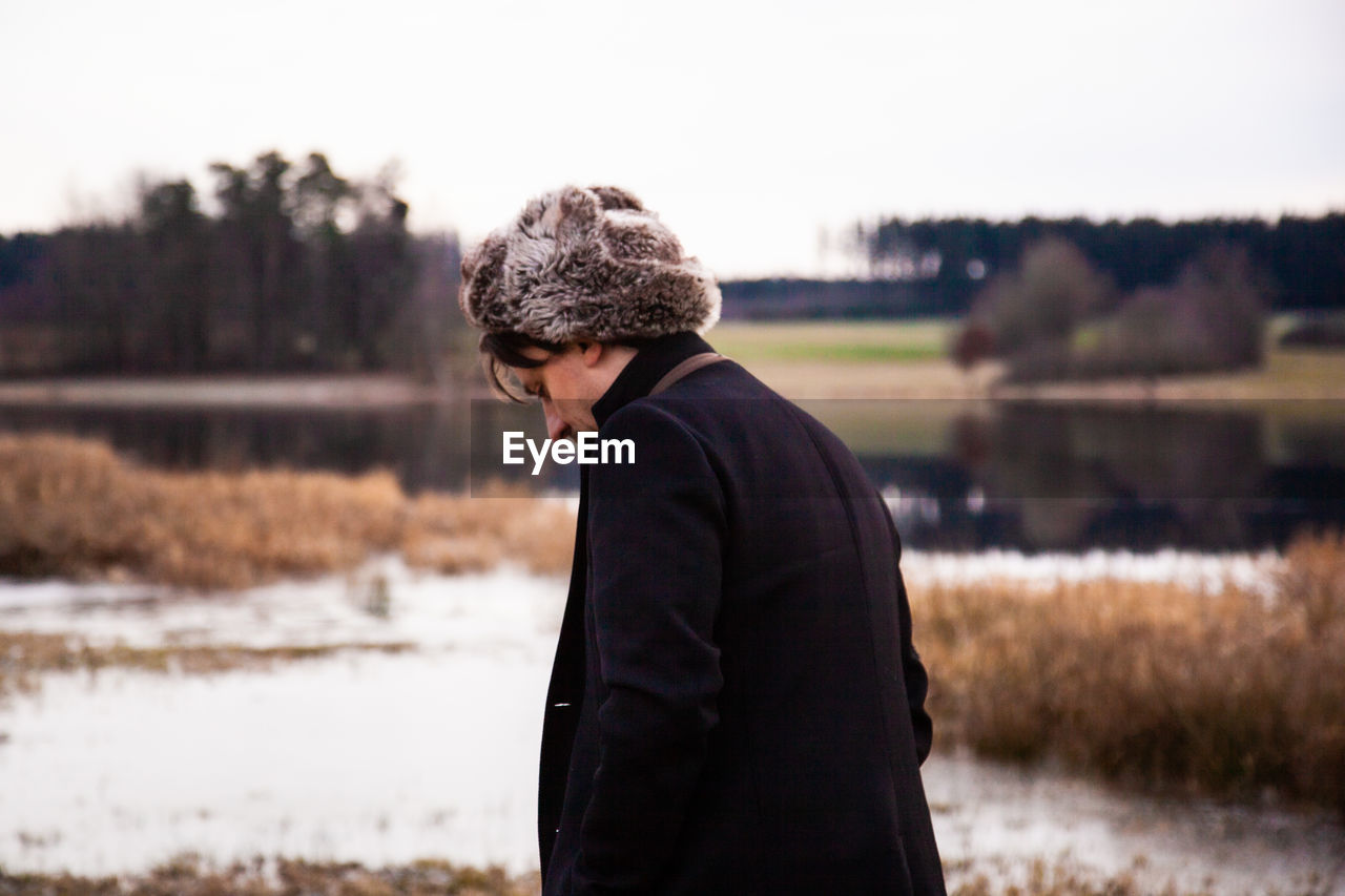 Man wearing fur hat standing on field against sky during winter