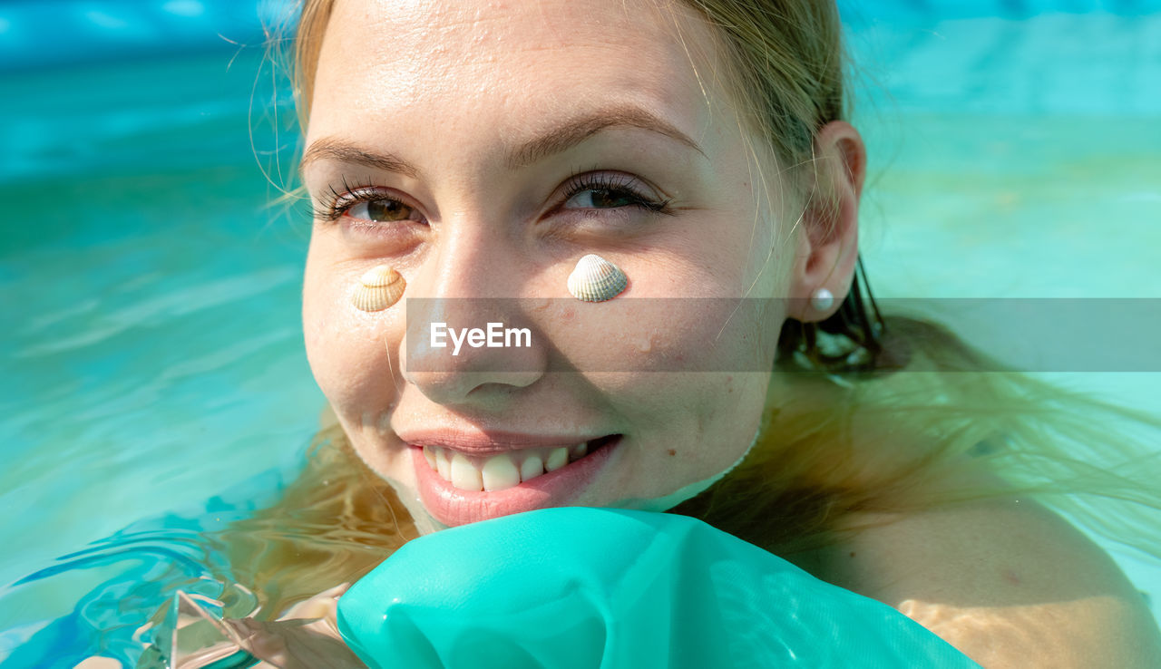 Portrait of smiling woman with seashells on face in swimming pool