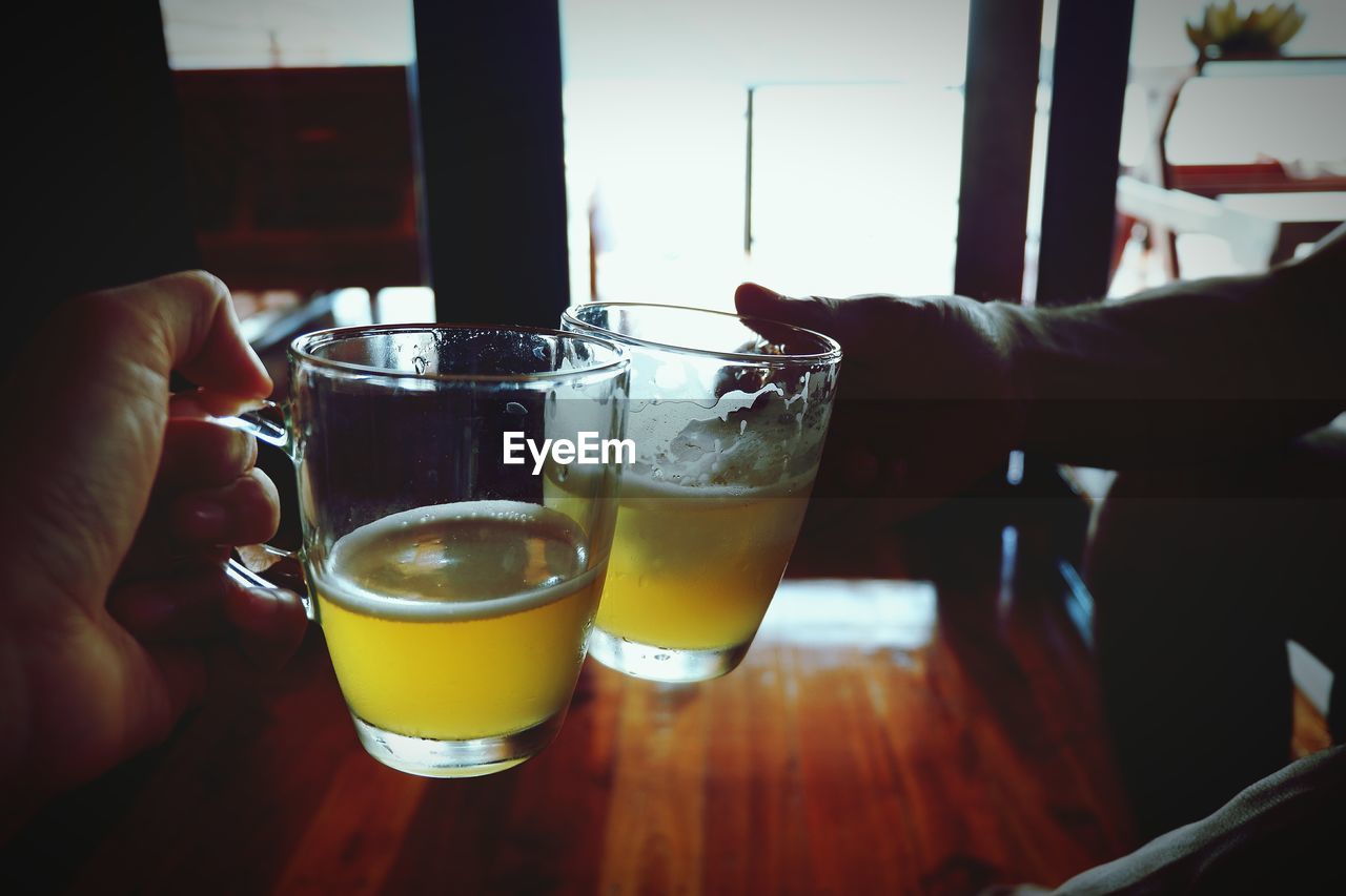 CLOSE-UP OF HAND HOLDING GLASS OF BEER ON TABLE