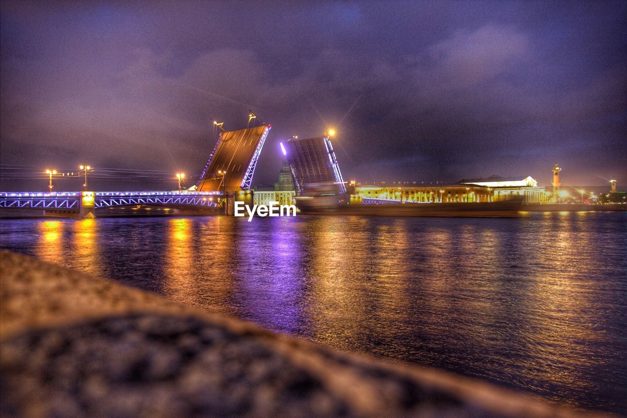 ILLUMINATED BRIDGE OVER RIVER AT NIGHT