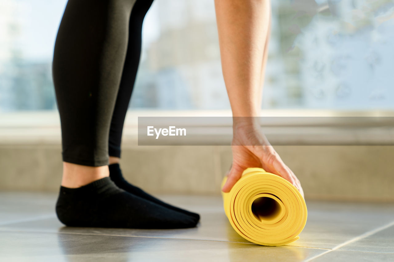 Young woman is preparing to unwrap yellow roll of sports mat for fitness, her hands lie on mat